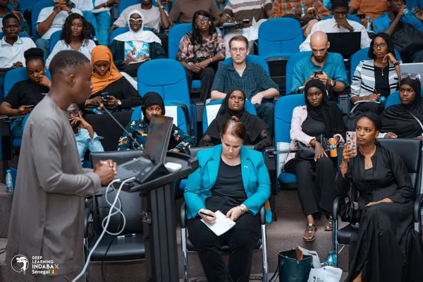 Un orateur au pupitre s'adresse à une salle attentive, plusieurs participants prennent des notes